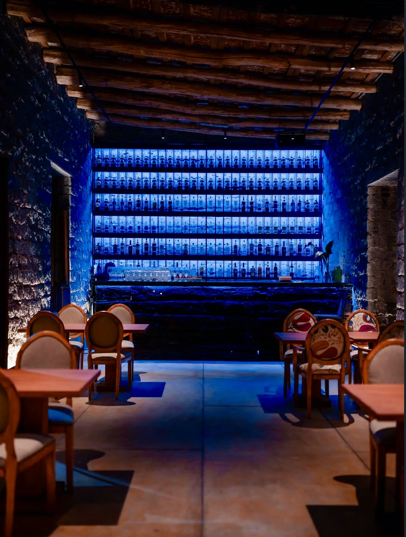 Barra de cócteles iluminada en azul con estantería de más de doscientas botellas